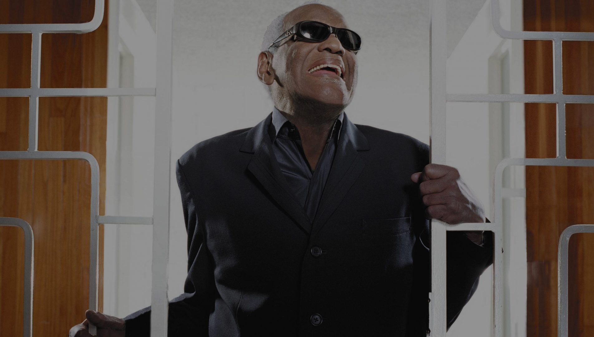 Ray Charles dressed in a black suit holding on to a decorative metal gate